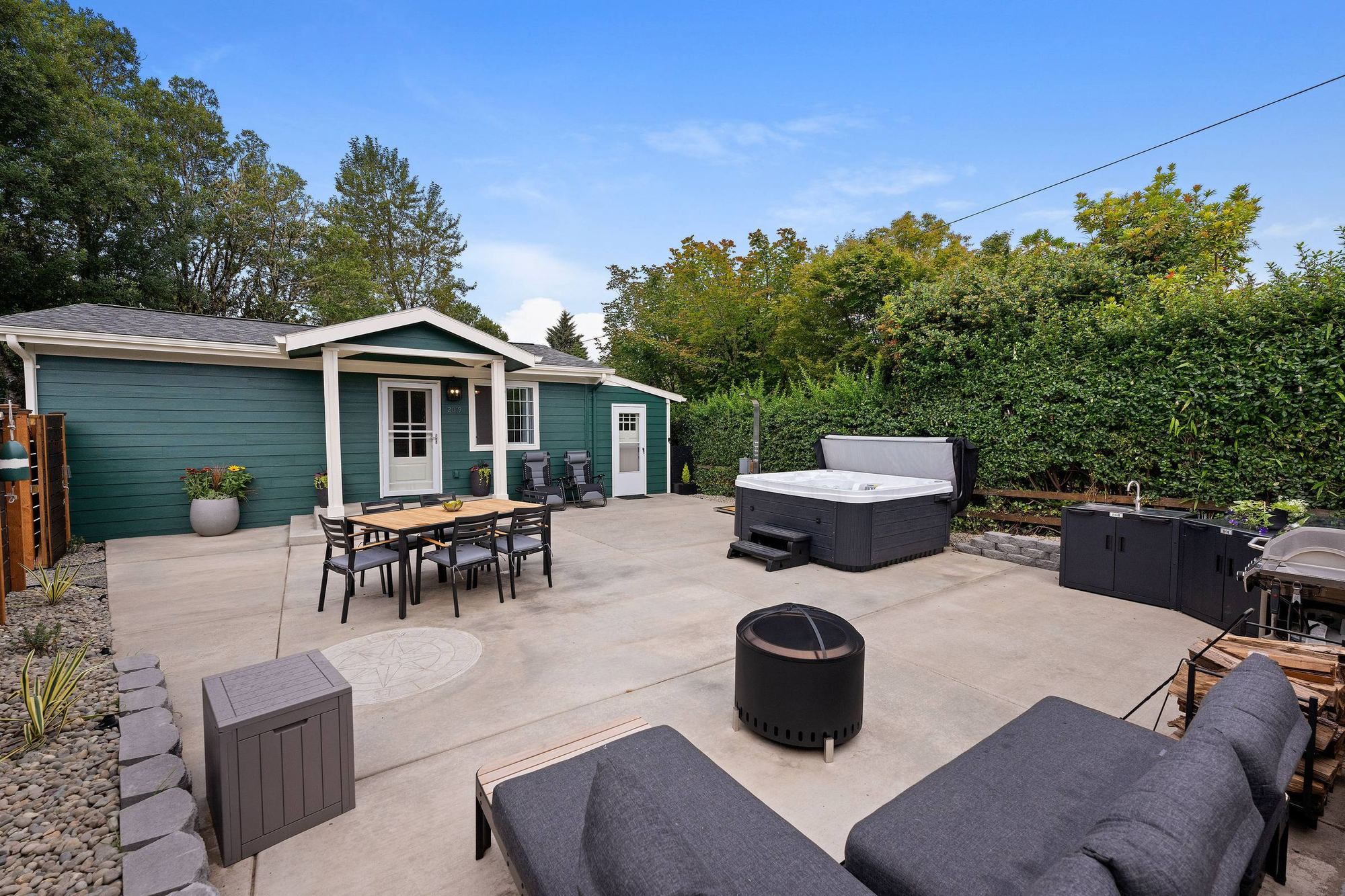 The courtyard by day: the cottage, dining table, hot tub, outdoor kitchen and fire pit lounge