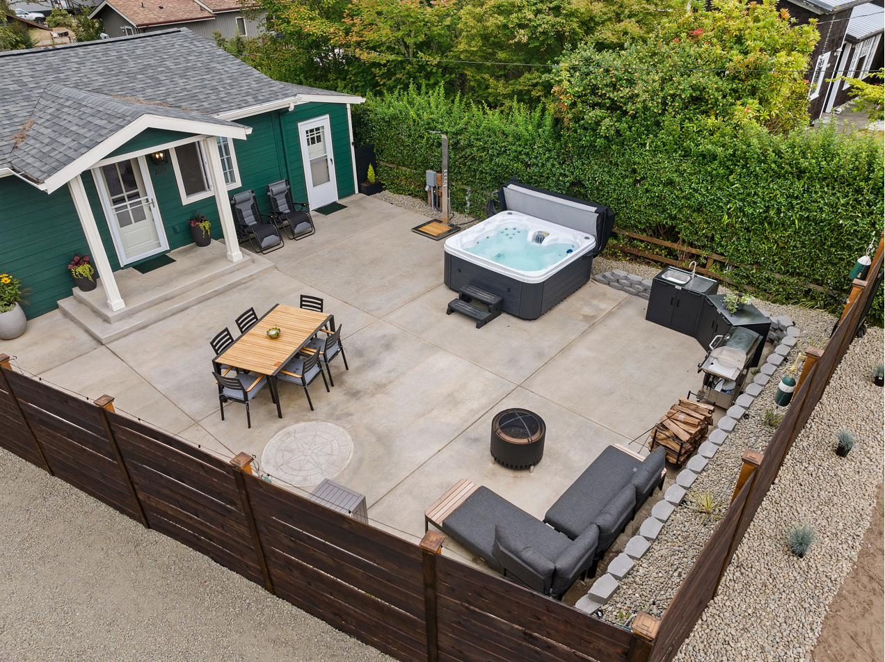 Aerial view of the fenced courtyard: hot tub, dining table, fire pit lounge and outdoor kitchen beside the cottage